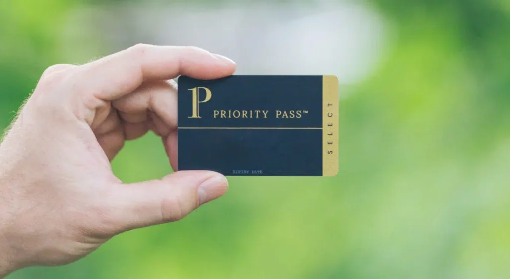 a hand holding a priority pass membership card in front of a green background.