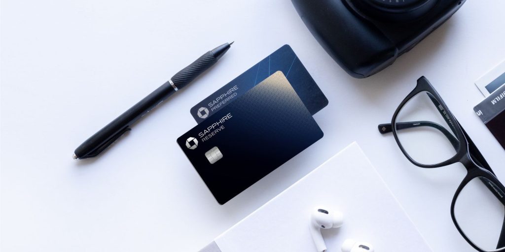 Chase Sapphire Preferred and Chase Sapphire Reserve cards on a table with a pen, camera, glasses, notebook, and airpods.